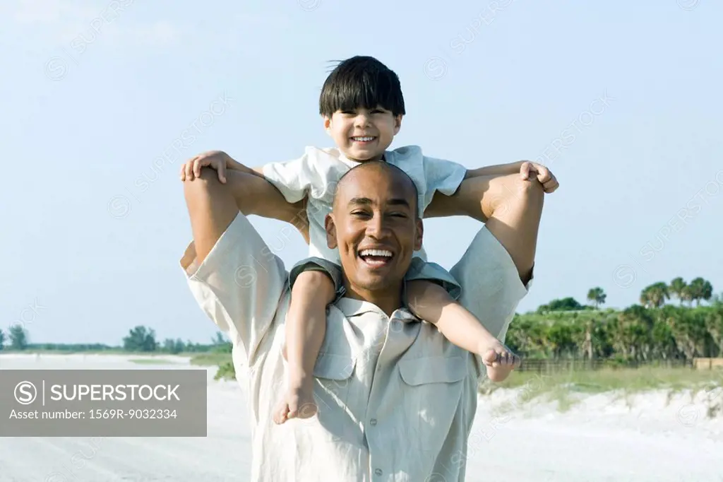 Father carrying son on shoulders, both smiling at camera