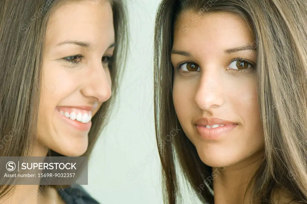 Two twin teenage sisters smiling, one looking at camera