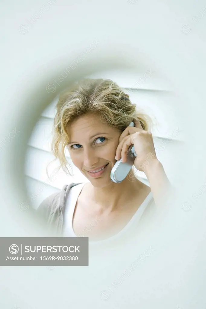 Woman using cell phone, smiling, viewed through hole