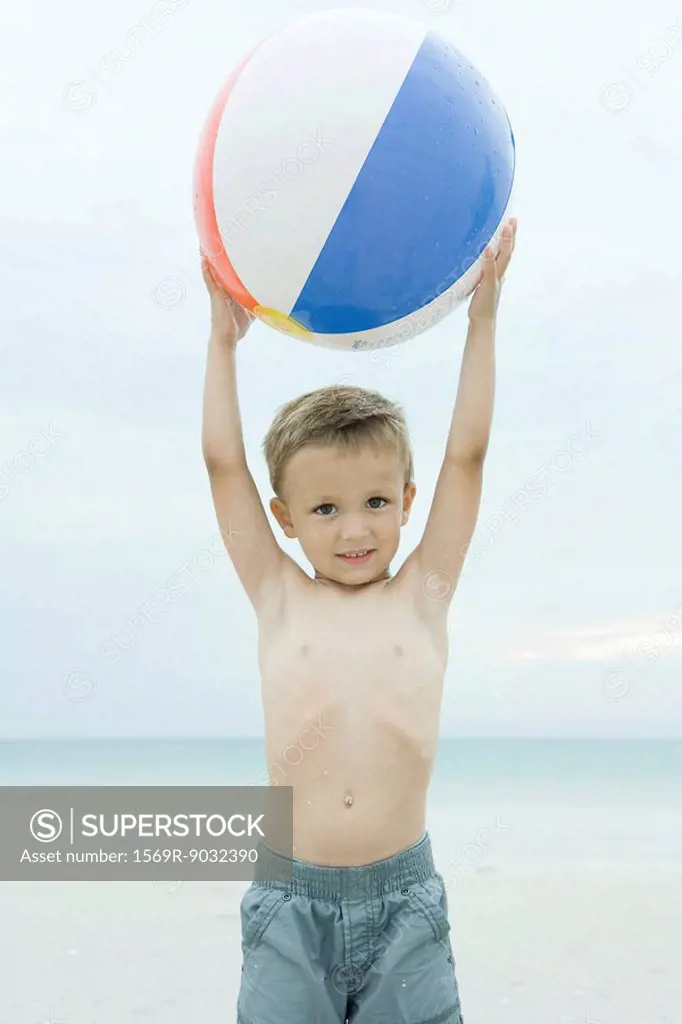 Little boy at the beach, holding up beach ball, smiling at camera