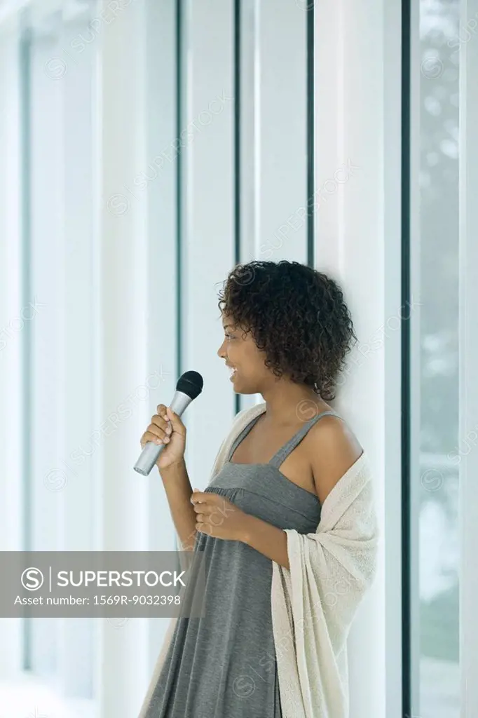 Young woman leaning against pole, singing into microphone, looking away