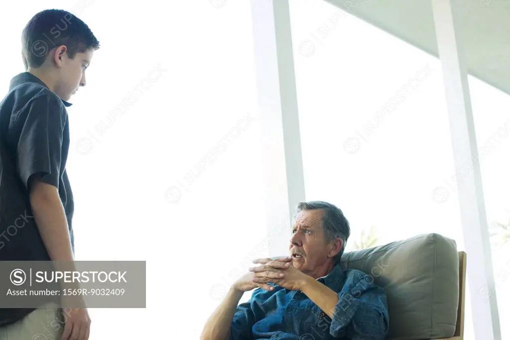 Grandfather talking with grandson on porch, hands clasped, both looking at each other