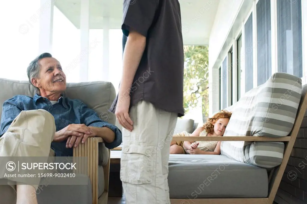 Grandfather and grandson talking on porch, little girl in the background looking at camera
