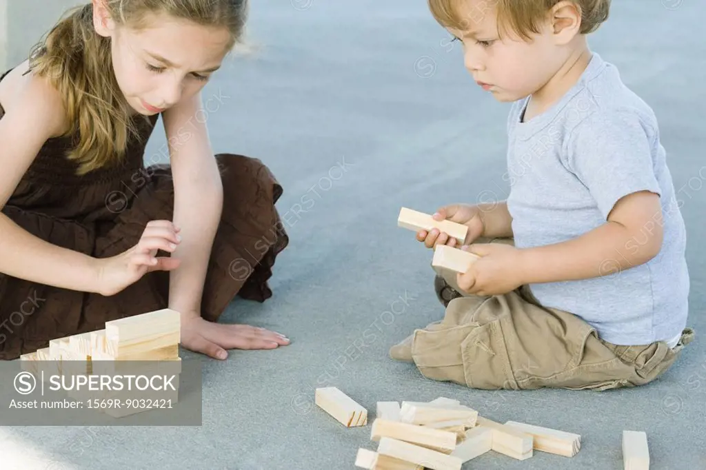 Brother and sister sitting on the ground, playing with building blocks together