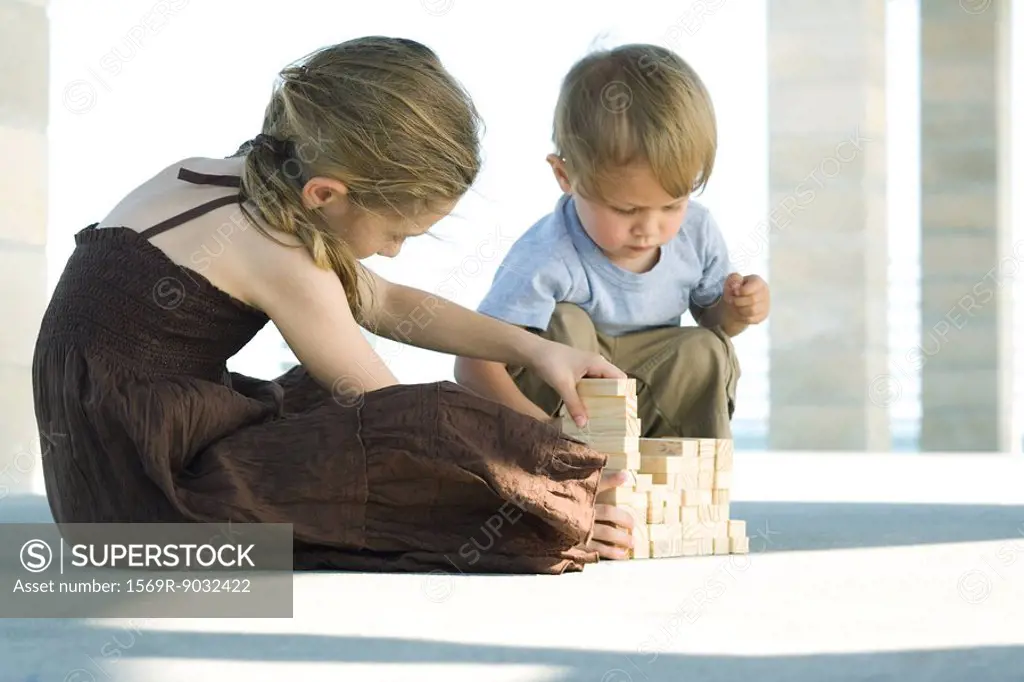Brother and sister sitting on the ground, stacking building blocks together