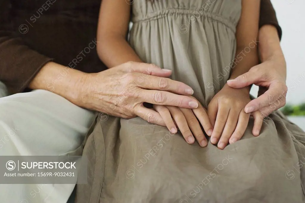 Woman embracing granddaughter, clasped hands, cropped view