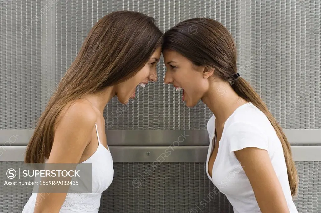 Teenage twin sisters leaning with foreheads touching, both shouting, side view
