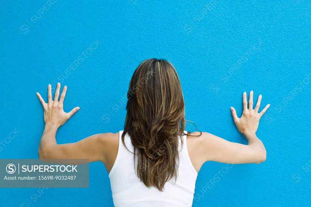 Woman standing with hands against blue wall, rear view