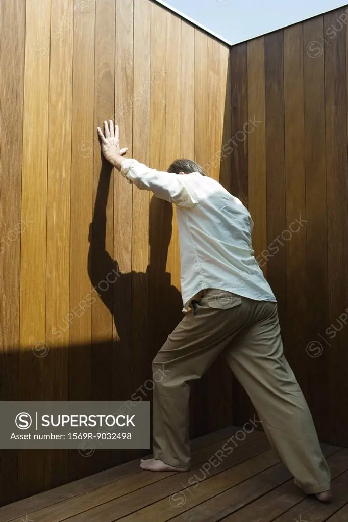 Man standing, pushing against wood paneling, side view