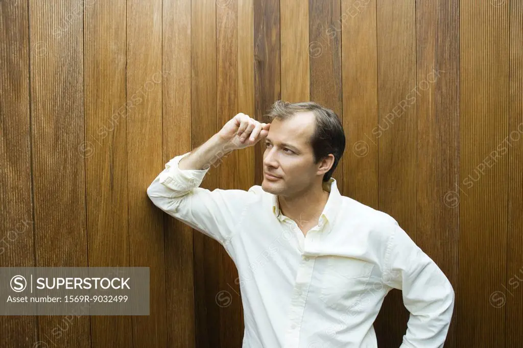 Man leaning elbow against wall, hand on head, looking away