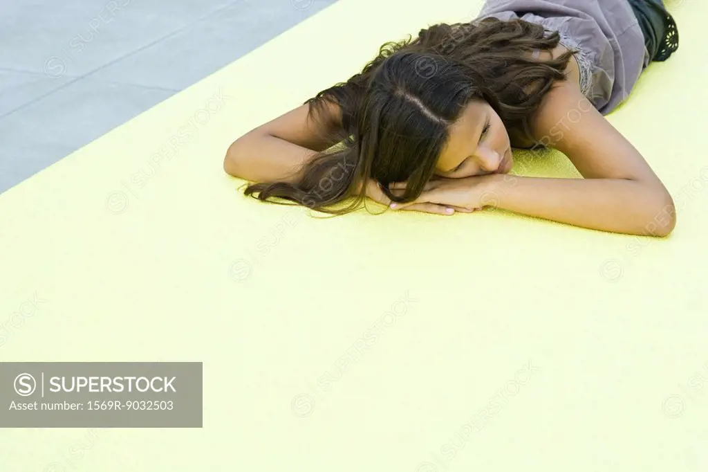 Teenage girl lying on stomach on the ground, head resting on arms