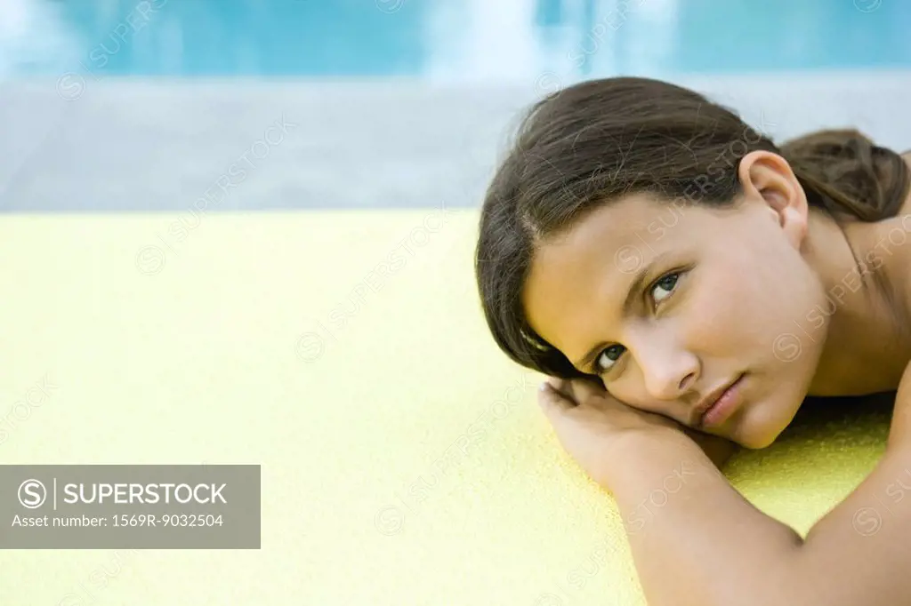 Teenage girl lying on stomach, head resting on arms, looking at camera