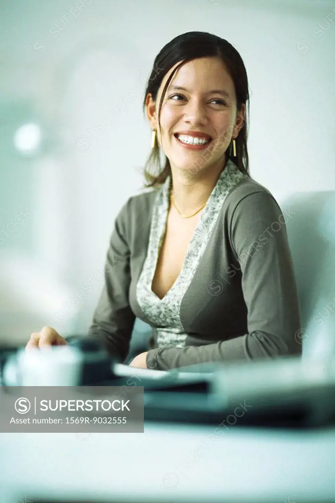 Woman sitting at desk, smiling, looking away