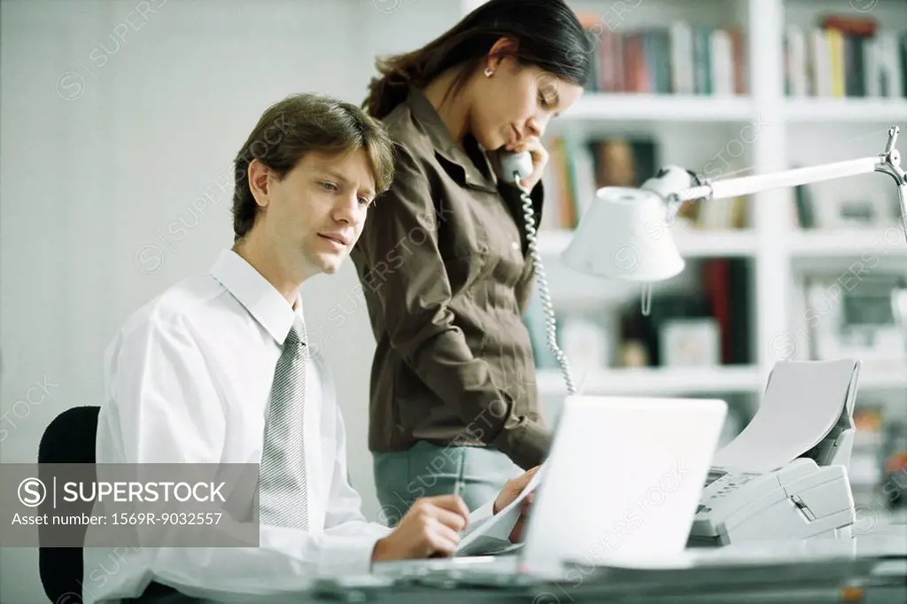 Male and female colleagues at desk, man using laptop computer, woman using phone