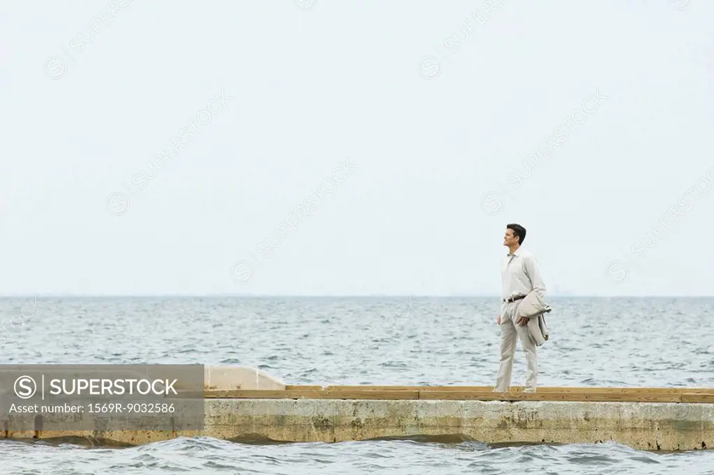 Man standing on jetty, looking at sea, in mid distance