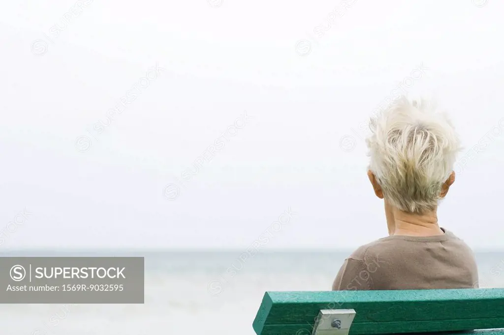Senior woman sitting near sea, rear view