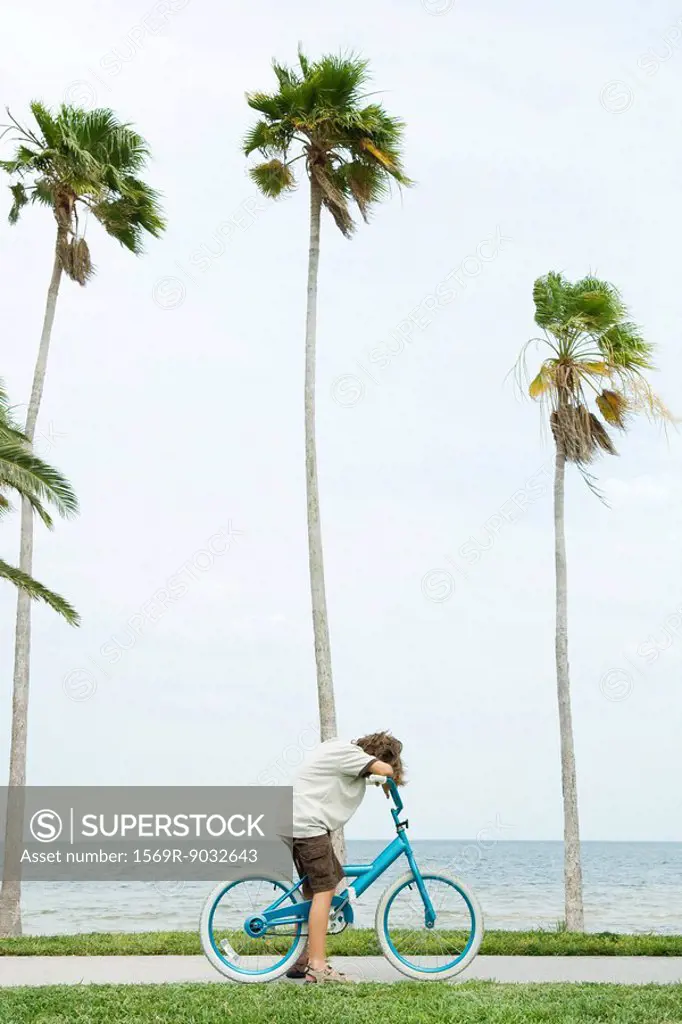Boy on bicycle at the beach, head resting on arms, side view