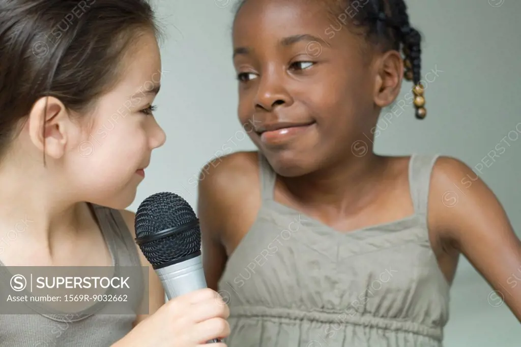 Two little girls smiling at each other, one holding microphone, close-up