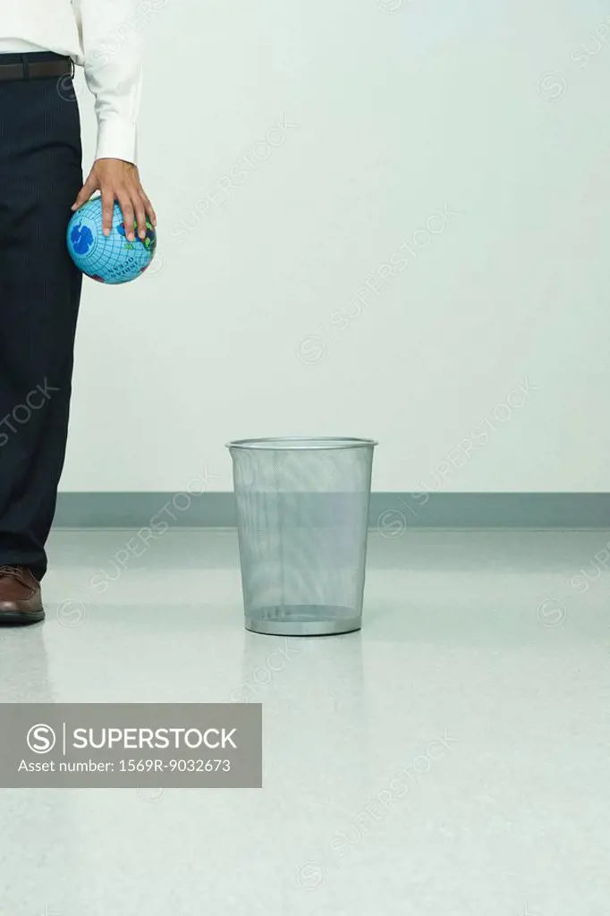 Man standing next to garbage can, holding globe in hand, cropped view