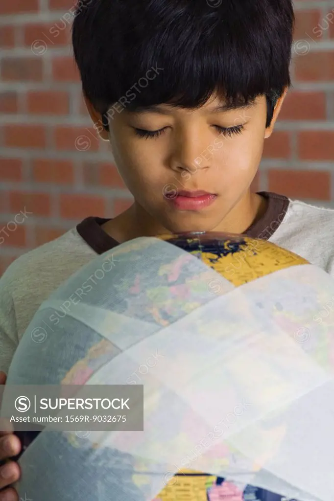 Boy holding globe wrapped in bandages, eyes closed, close-up