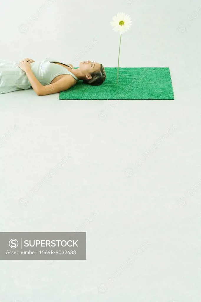 Woman lying on artificial turf next to gerbera daisy, looking up