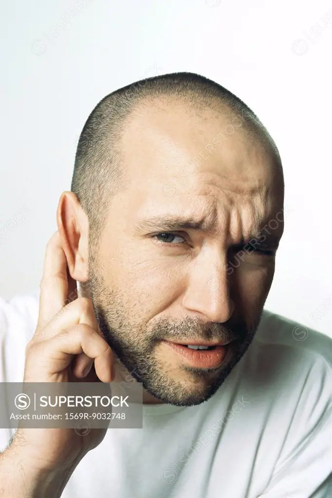 Man holding ear, furrowing brow, looking at camera, close-up