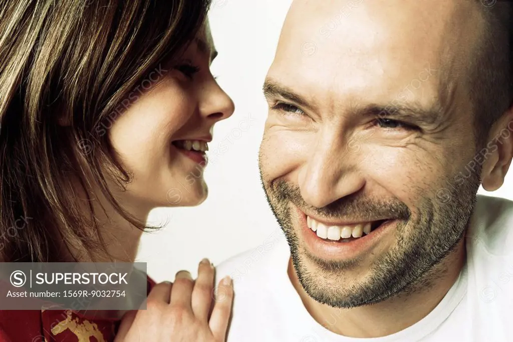 Woman whispering into man´s ear, both smiling, close-up