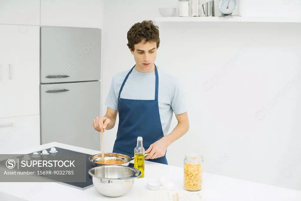 Man standing at stove, cooking, looking down at recipe