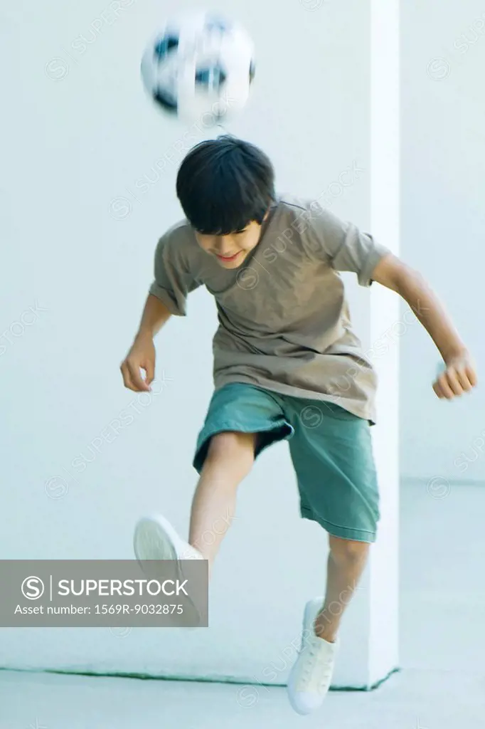 Little boy playing with soccer ball, jumping, head down