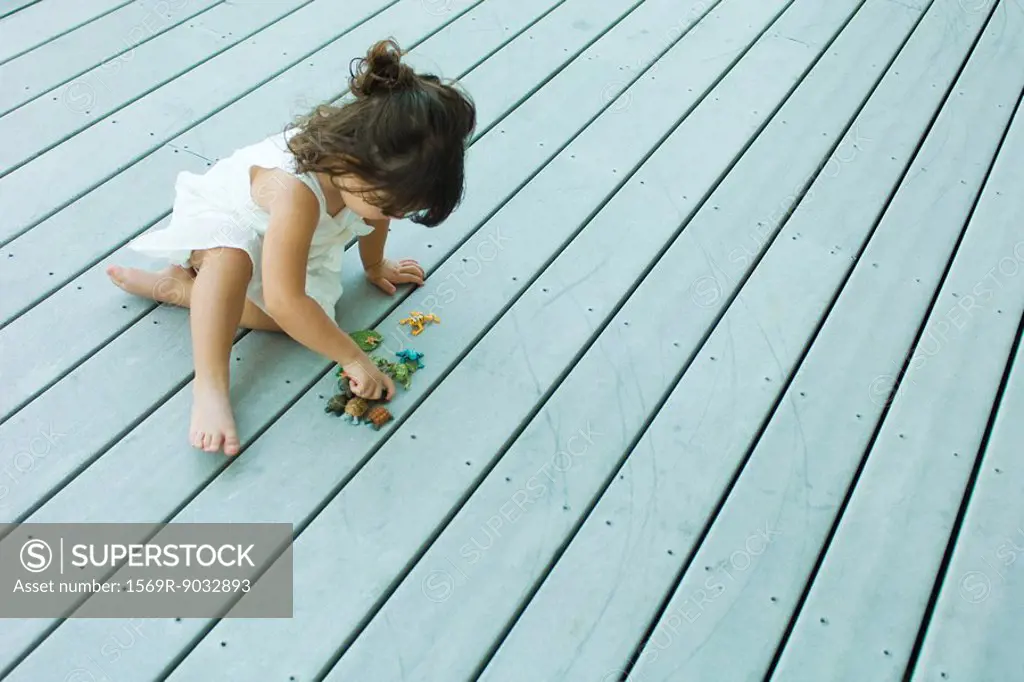 Little girl sitting on deck, playing with plastic toys, high angle view
