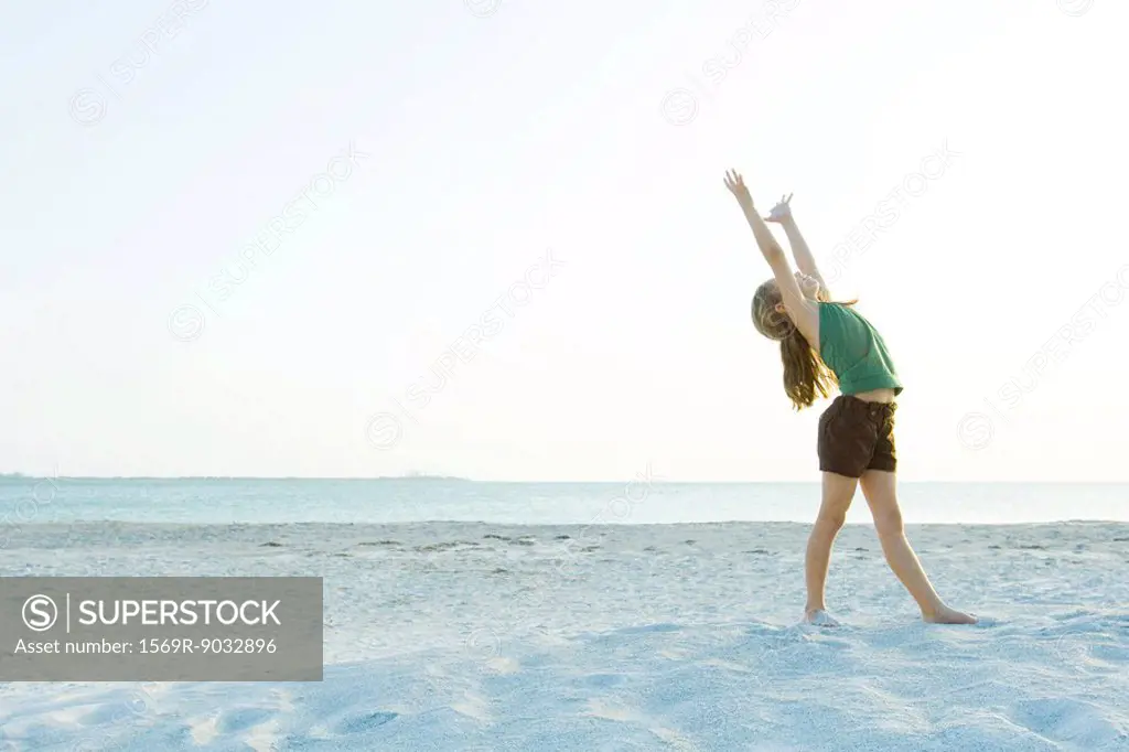 Little girl standing on the beach with arms raised, head back, full length