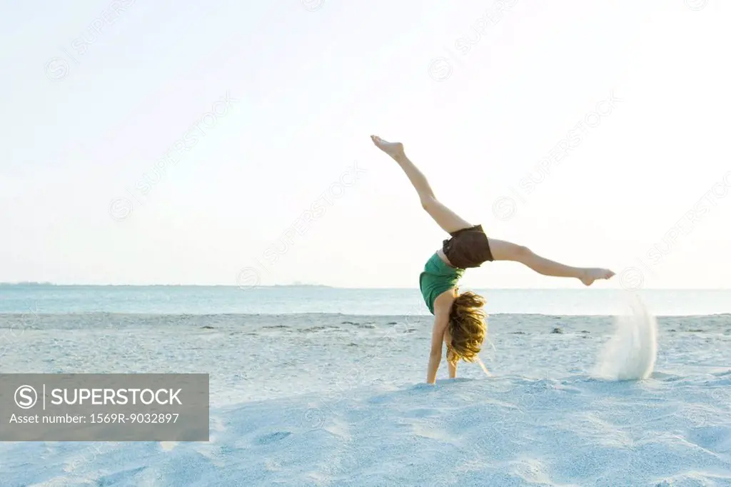 Little girl doing handstand at the beach, side view