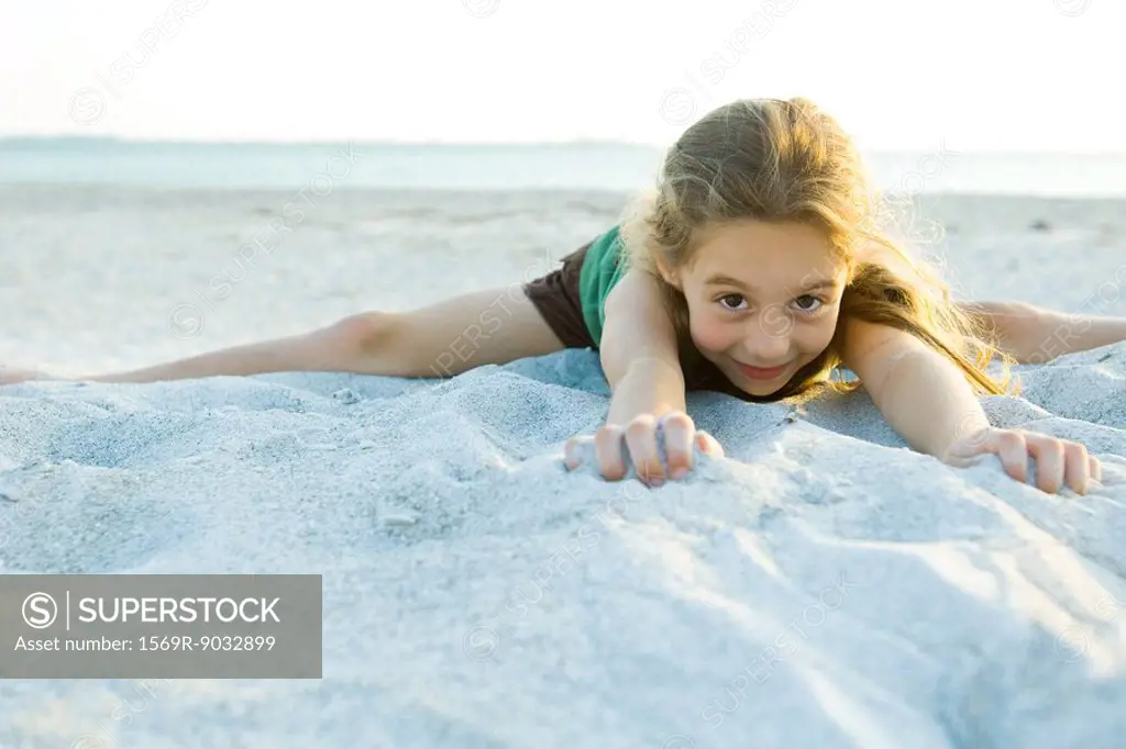 Little girl lying in sand at the beach, smiling at camera