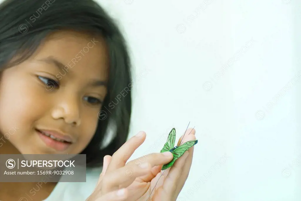 Little girl touching butterfly, looking down, smiling