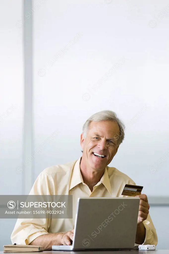 Man using laptop computer, holding credit card, smiling at camera