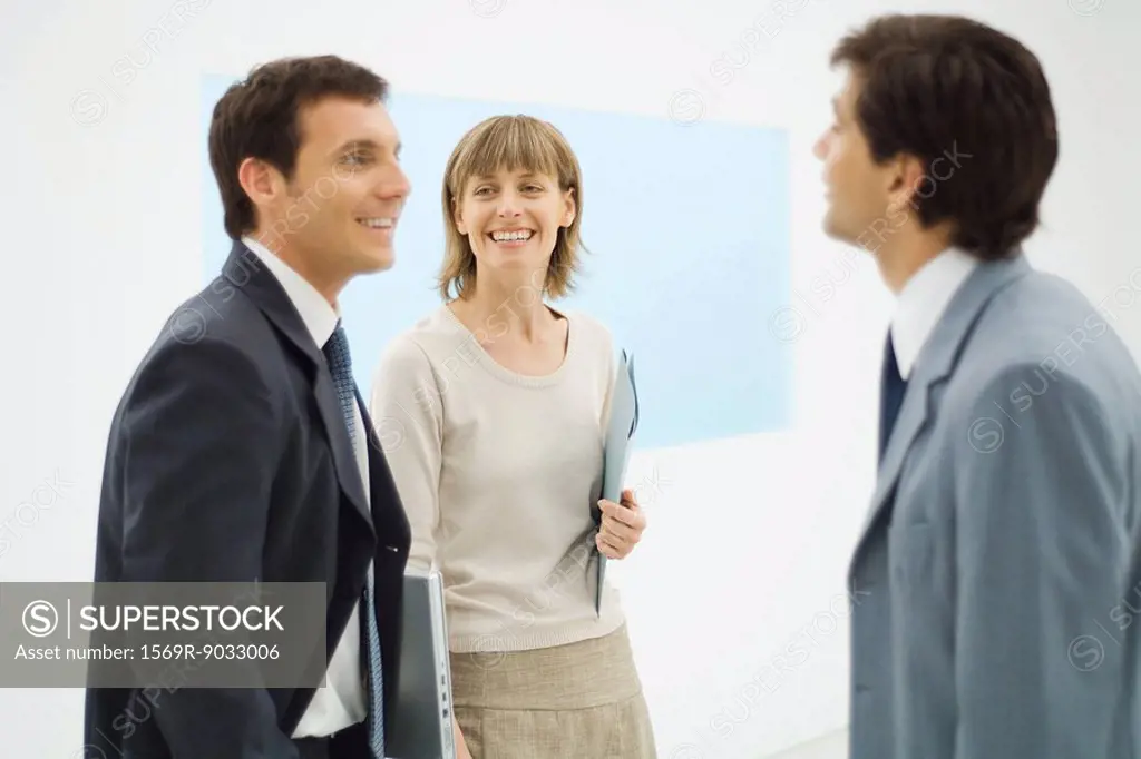 Three business associates standing together, having a discussion, smiling