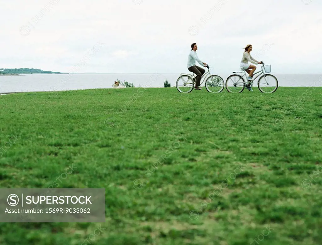 Couple riding bicycles at water´s edge, mid-distance
