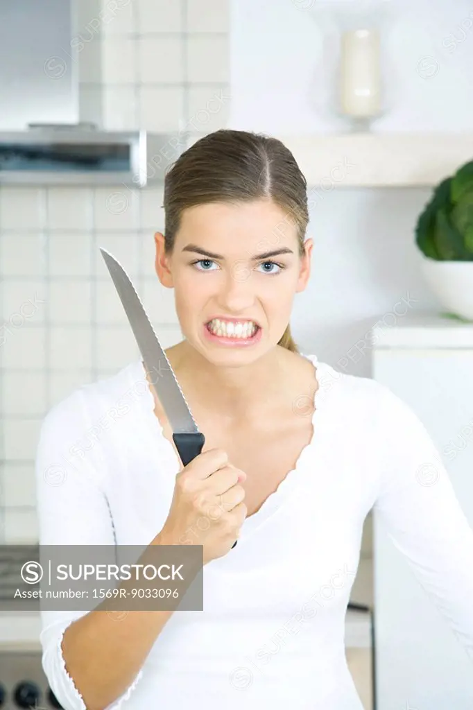 Woman holding up kitchen knife, clenching teeth, looking at camera, portrait
