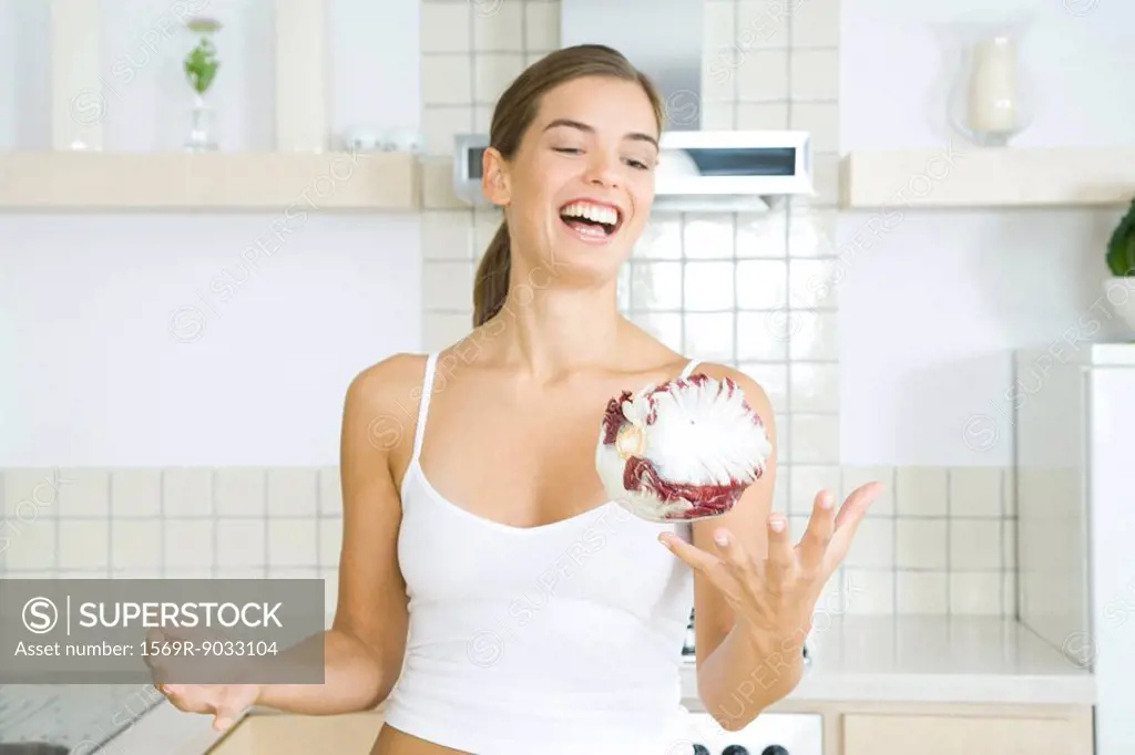 Young woman in kitchen, tossing chicory in the air, laughing