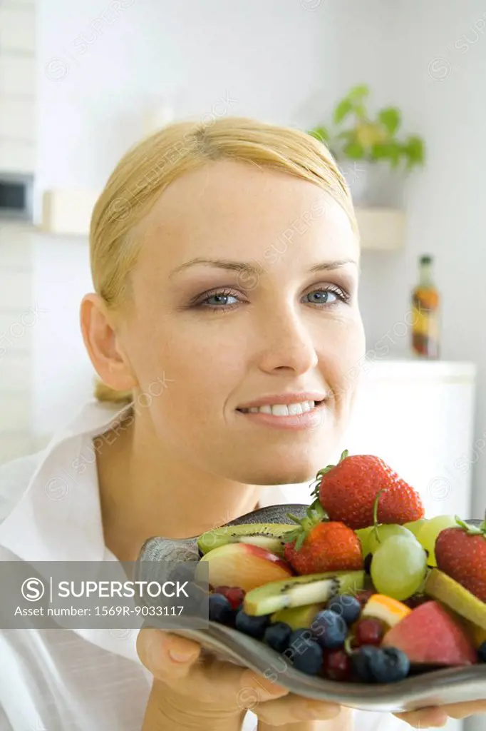 Woman holding assorted fruits on plate, smiling at camera