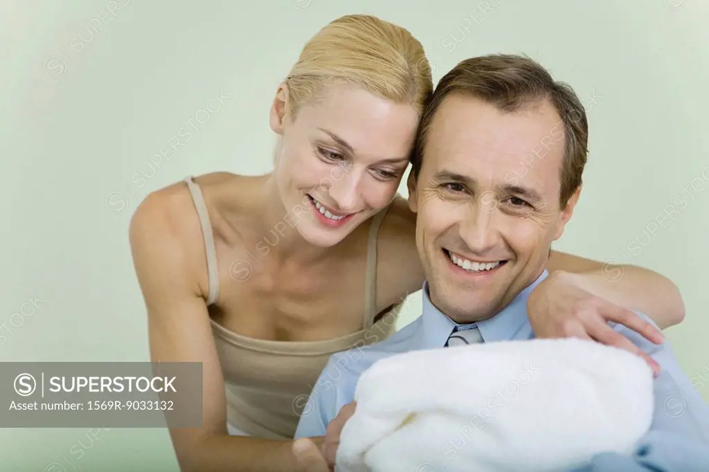 Couple holding new baby wrapped in blanket, smiling, man looking at camera