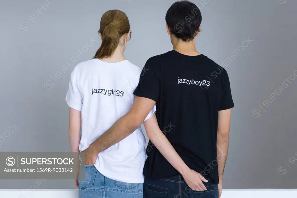 Young couple wearing customized tee-shirts, arms around each other´s waists, rear view