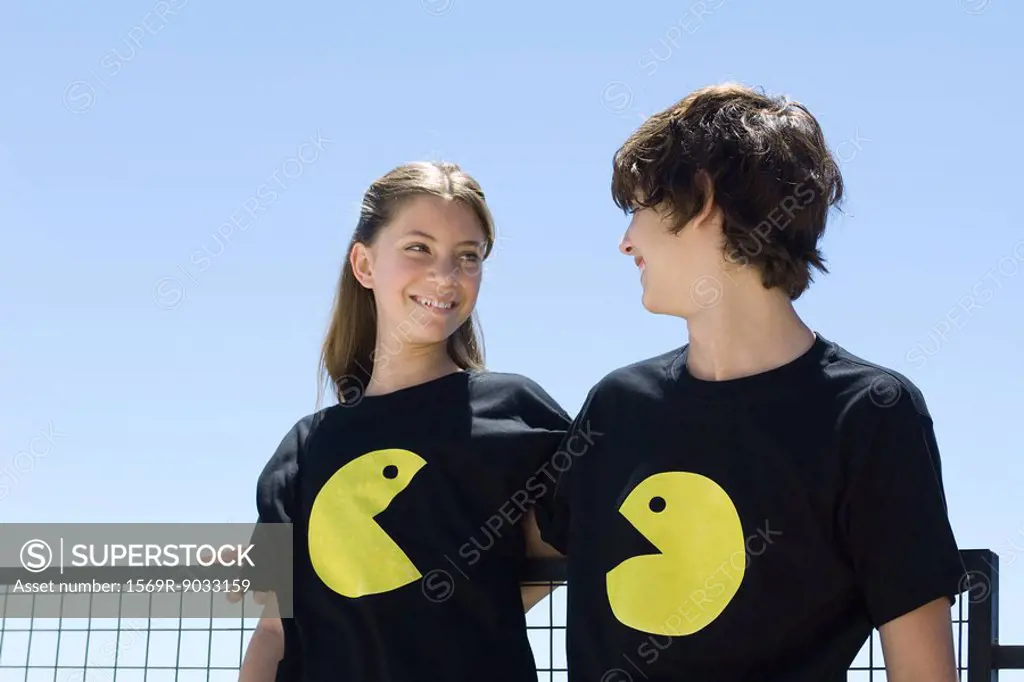 Young couple wearing tee-shirts printed with graphic characters, smiling at each other
