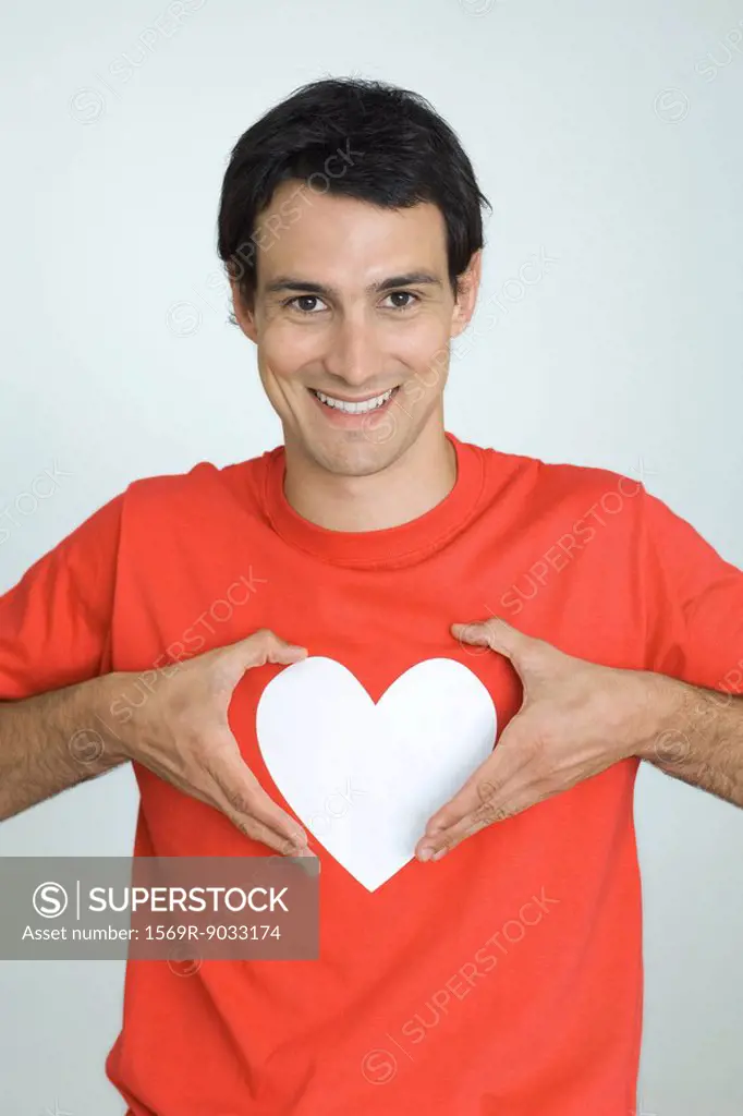 Man wearing tee-shirt with heart symbol, holding hands around heart, smiling at camera