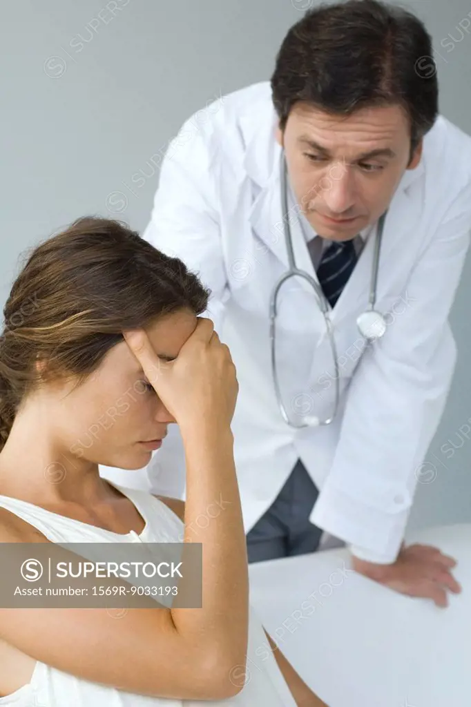 Male doctor examining patient, woman sitting with hand over eyes