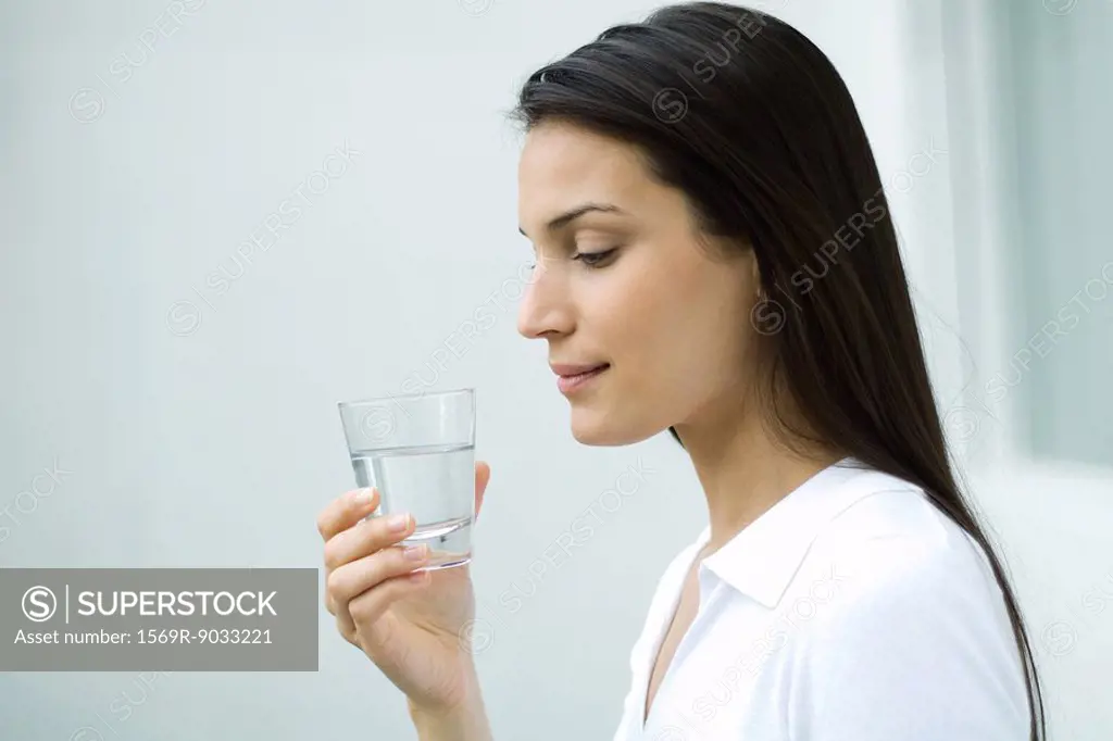 Woman holding glass of water, looking down, side view