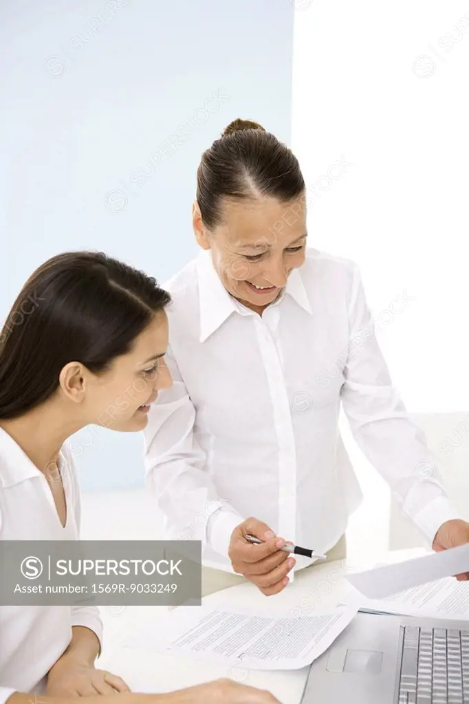 Senior woman working with younger colleague in office, smiling