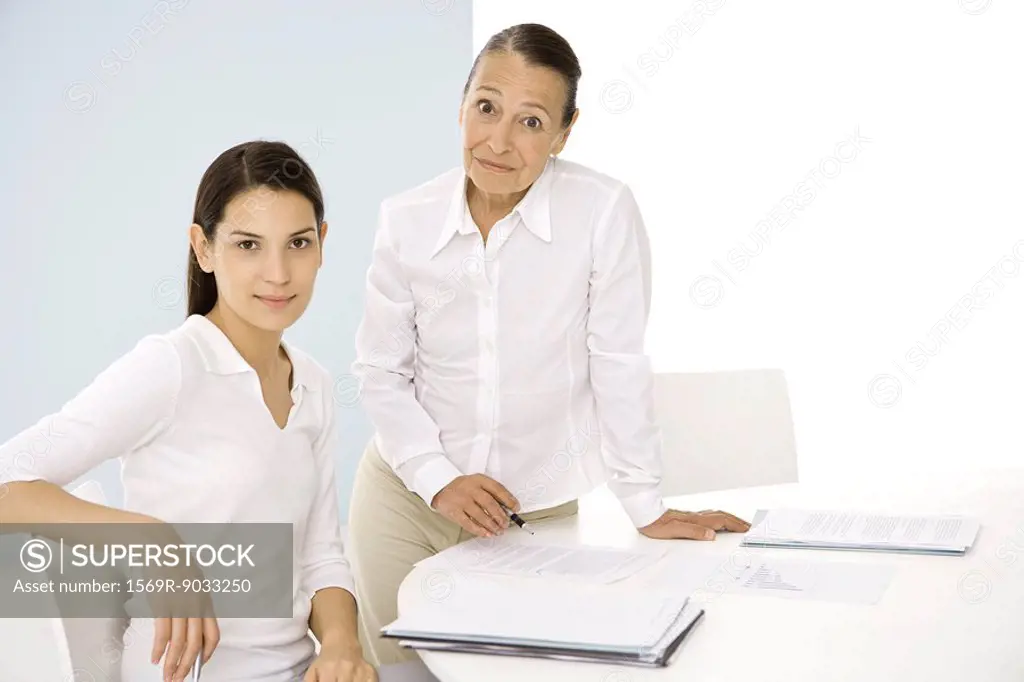 Senior woman with younger colleague in office, both smiling at camera