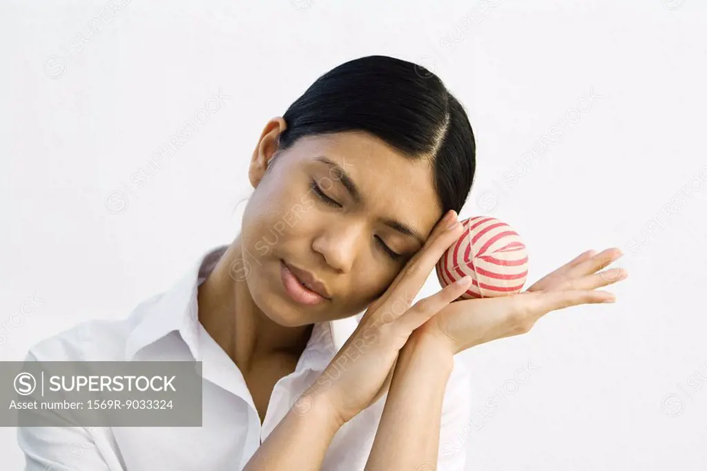 Young woman resting head on hands, holding ball, eyes closed