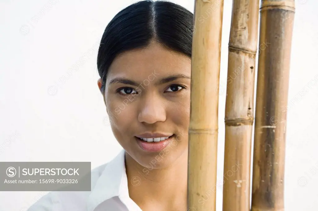 Woman standing behind bamboo stacks, looking at camera, portrait